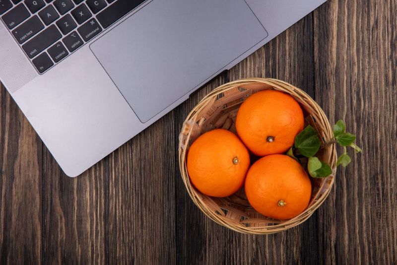 laptop with some oranges next to inside of a little whicker bowl